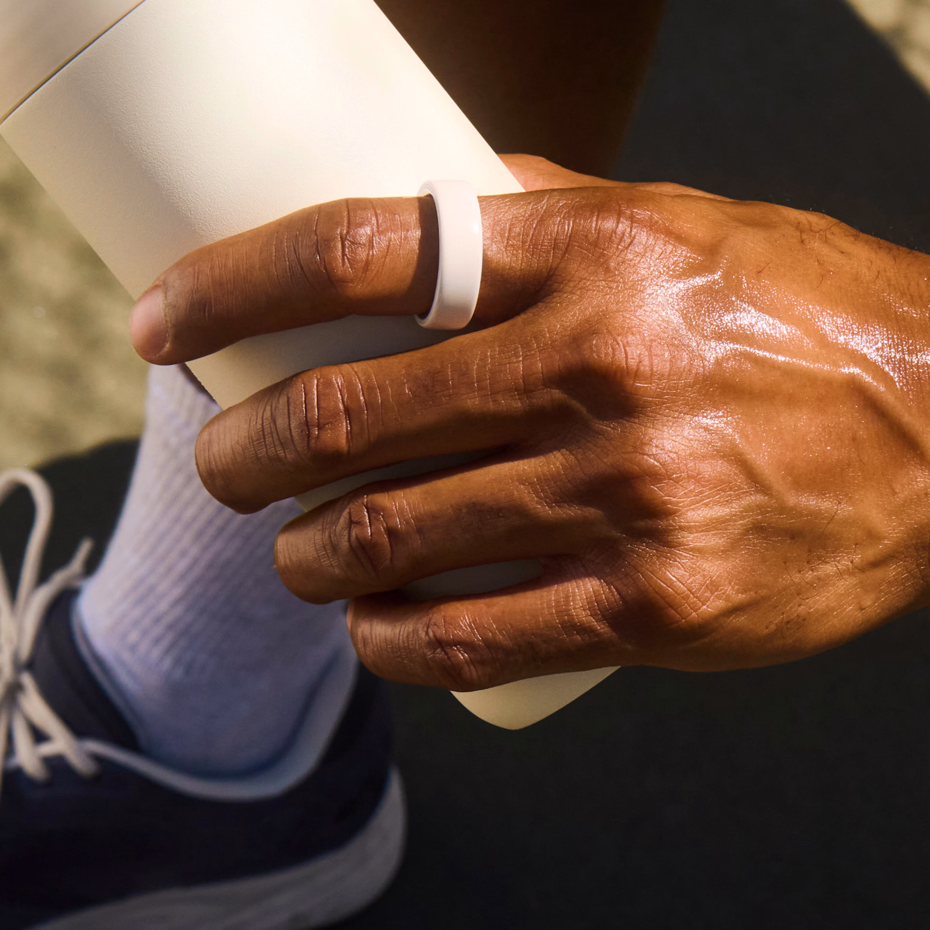 A person wearing a Cloud Oura Ring 4 Ceramic holds a water bottle